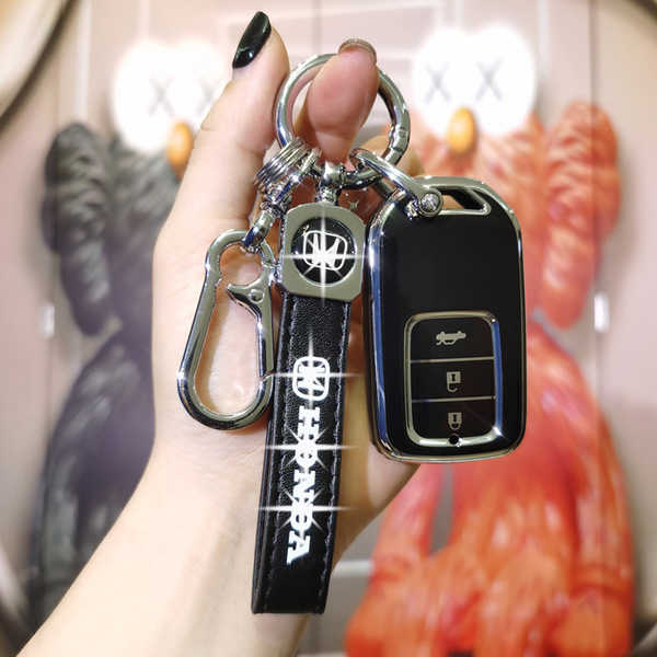 A hand holds a sleek black key cover for the 2024 honda cr-v, hr-v, and 2023 breeze, featuring a shiny honda logo and a match...
