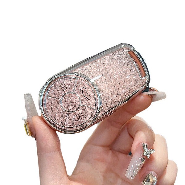 A hand holds a sparkling pink ora good cat key cover, featuring a glittery texture and silver trim, designed for the ballet c...