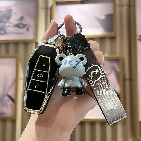A hand holds an icar 03 key cover for eq7 shuxiangjia 2024, featuring a sleek black design with silver accents and a playful ...