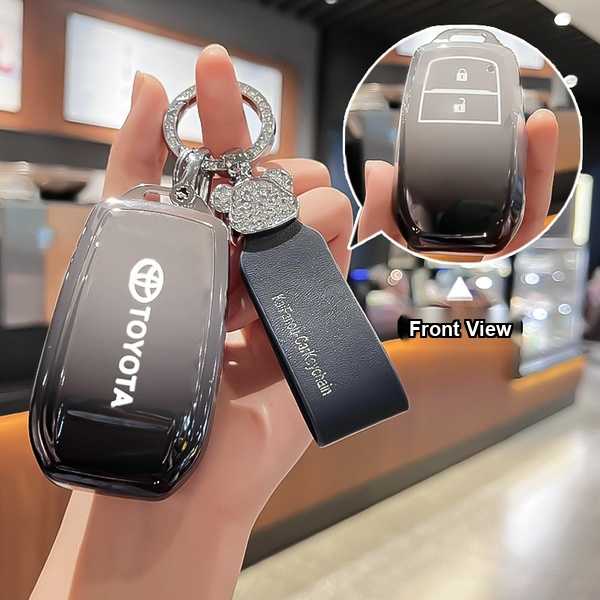 Hand holding a sleek black leather toyota crown kluger key cover, featuring a front view with a diamond-embellished keychain ...