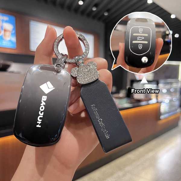 A hand holds a sleek baojun 730 key cover, featuring a shiny black leather design with a sparkling emblem and a clear front v...