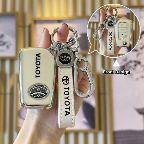 A hand holds a cream-colored toyota key cover with the brand logo and toyota text, featuring a matching strap and carabiner, ...