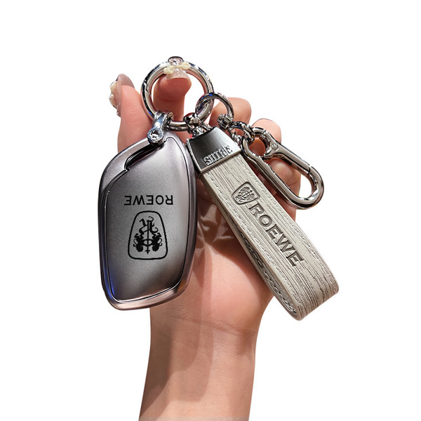 A hand holds a sleek roewe rx5 key cover, featuring a metallic finish and leather strap with the roewe logo, designed as a pr...