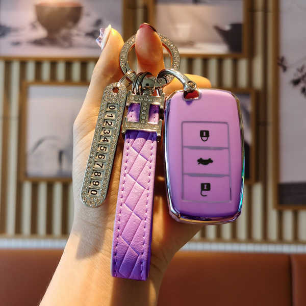 A hand holds a stylish purple lufeng x2 key cover with a quilted strap and a decorative keychain, designed for 2017 models.