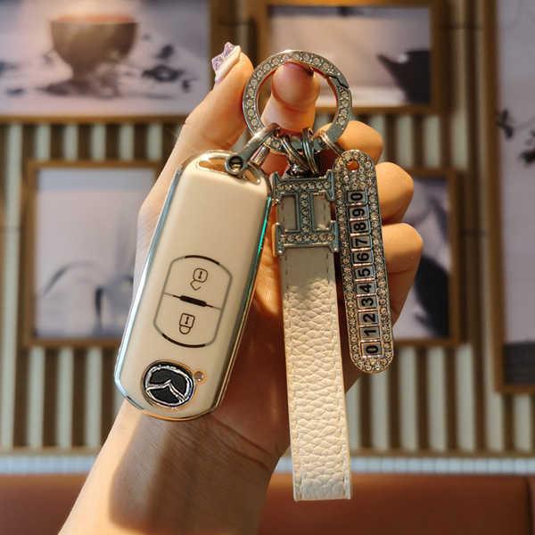 A hand holds a mazda 3 key cover, featuring a slim leather shell with a decorative keychain and a sleek design for cx-3/cx-5/...