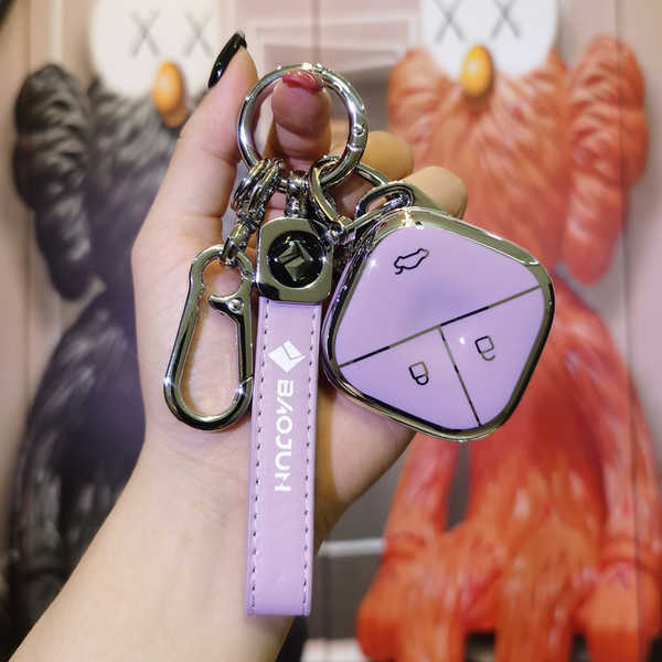 A hand holds a stylish purple baojun kiwi ev key cover, featuring a sleek design with a car icon and lock symbol, set against...