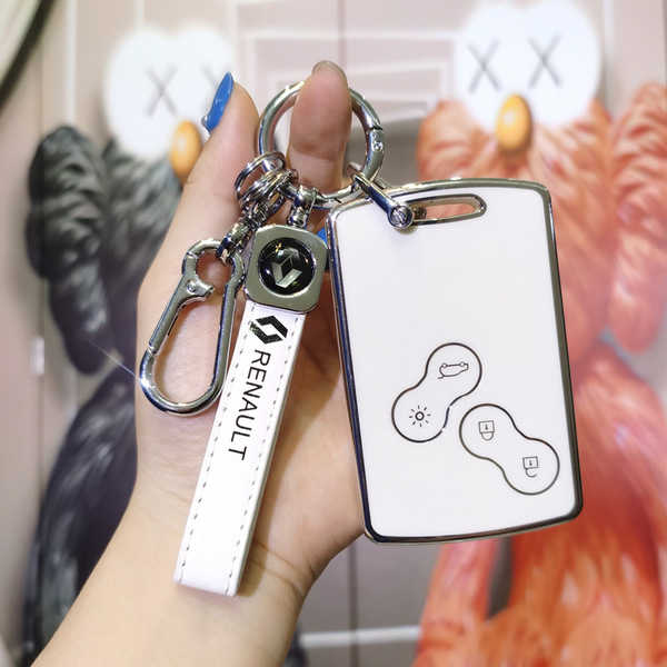 A hand holds a sleek white renault key cover, featuring a car icon and lock symbol, designed for koleos, megane, and talisman...