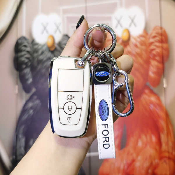 A hand holds a white ford key fob with a leather strap and carabiner, set against a vibrant backdrop featuring artistic bear ...