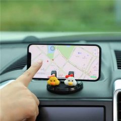 A hand points to a smartphone mounted on a dashboard using a swan car phone holder, featuring two cute duck-shaped stands for...