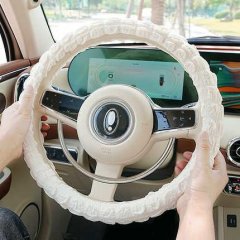 A person holds a cars steering wheel wrapped in a white, textured goddess puff steering wheel cover, designed for non-slip gr...