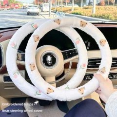 A hand holds a plush, white steering wheel cover adorned with embroidered bears and tulips, offering warmth and a non-slip gr...
