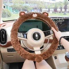 A hand holds a cozy, brown, bear-themed steering wheel cover with soft, frosted rabbit fur texture, designed for non-slip gri...