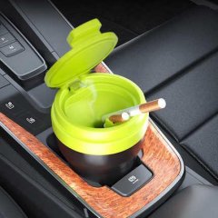 Portable car ashtray with lid, featuring a green and black design, placed in a cars cup holder, holding a cigarette.