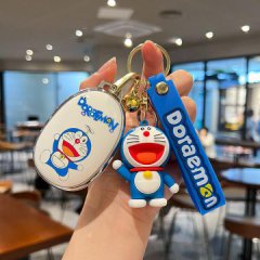 Hand holding a doraemon-themed car key cover and accessories, featuring a white oval case with doraemons image, a blue keycha...