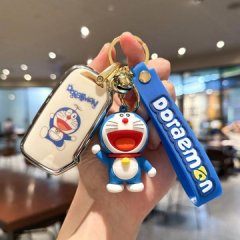 A hand holds a doraemon-themed key cover and accessories, featuring a white leather case with a doraemon print, a blue doraem...