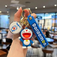 A hand holds a set of doraemon-themed keychains, featuring a round charm with doraemons face and a blue strap with doraemon t...