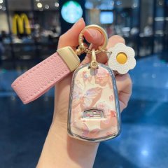 A hand holds a cadillac xt5 key cover featuring a floral design with butterflies, a pink leather strap, and a daisy-shaped ch...