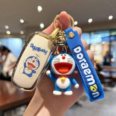 A hand holds a geely panda mini car key cover featuring a cute doraemon design, complete with a matching keychain and strap, ...