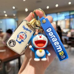 A hand holds a doraemon-themed key cover and accessories, featuring a blue and white design with the iconic character and dor...