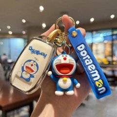 A hand holds a doraemon-themed key cover and matching keychain, featuring a cheerful doraemon design on a white case and a bl...