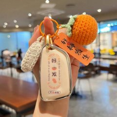 A hand holds a cadillac xt5 car key cover with a (good fortune) design, accompanied by a crocheted orange fruit charm and ...