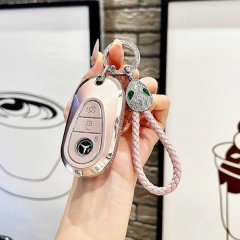A hand holds a sleek, rose-gold mercedes c260l key cover for 2025 models, featuring a braided pink strap and a decorative key...