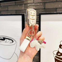 A hand holds a cadillac xt5 key cover featuring premium leather with a gold-accented design, adorned with a white horse-shape...