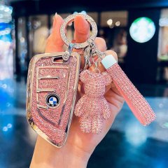 A hand holds a sparkling pink bmw key cover for x3, x1, x2, 3 series, 325li, and i3, featuring a glittery design, a teddy bea...