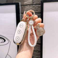 A hand holds a stylish ideal l8 key cover, featuring a white leather design with gold accents and a decorative charm, perfect...