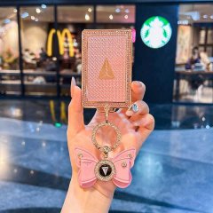 A hand holds a pink, diamond-embellished changan deep blue s7 card key cover with a butterfly charm and gold logo, set agains...