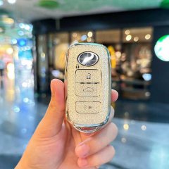 A hand holds a north deer tp-1 tpu car key cover, showcasing its glittery gold finish and sleek design with lock, unlock, and...