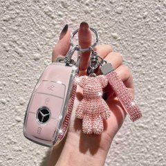 A hand holds a pink mercedes-benz key cover adorned with rhinestones, featuring a matching teddy bear charm and strap, design...