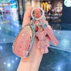 A hand holds a stylish wey blue mountain key cover for dht-phev 2024, featuring a glittery pink design with a sparkling teddy...