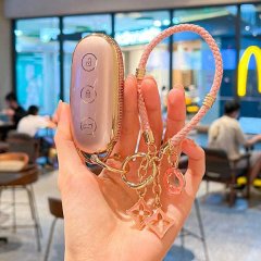 A hand holds a sleek, gold-accented ideal l6 key cover 2025, featuring a pink leather strap and decorative charms, set agains...
