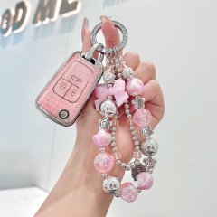 A hand holds a pink chevrolet key cover for cruze, malibu xl & trax, adorned with a decorative keychain featuring beads and c...