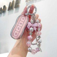 A hand holds a xiaomi su7 key cover with a glittery pink design and a decorative keychain featuring beads, a bow, and metalli...