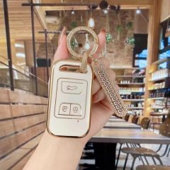 A hand holds a stylish chery qq ice cream key cover, featuring a gold-trimmed white design with a sparkling keychain, set aga...