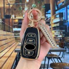 A hand holds a sleek, black and gold subaru forester key cover with a decorative keychain, showcasing its premium design in a...