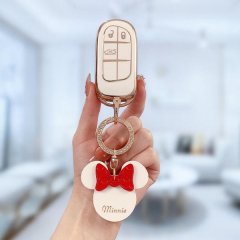 A hand holds a jeep compass key cover featuring a minnie mouse design with a red bow and minnie text, set against a bright, m...