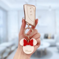 A hand holds a lexus es200 key cover with a minnie mouse charm, featuring a red bow and minnie text, set against a bright, mo...