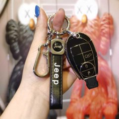 A hand holds a jeep key cover designed for older models, featuring a sleek black leather strap with jeep text and a matching ...