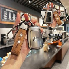 Hand holding a toyota key cover with leather strap, showcasing front view in a cafe setting.