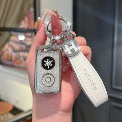 A hand holds a stylish yamaha nmax155/xmax300 key cover, featuring a sleek silver design with a snowflake logo and power butt...