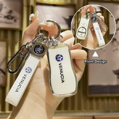A hand holds a white venucia key cover with a sleek design, featuring the brand logo and a matching keychain, showcased again...