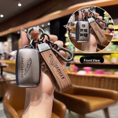 A hand holds a jaguar key cover with a leather strap, showcasing its sleek design and front view in a cozy cafe setting.