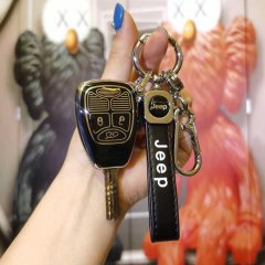 A hand holds a sleek black jeep compass key cover with gold accents, featuring a matching keychain and strap, set against a v...