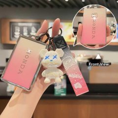 Hand holding a pink honda civic type r key cover with a bear charm, showcasing the front view in a cafe setting.