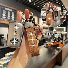 A hand holds a toyota key cover with a wooden strap, showcasing its front view in a cozy cafe setting. the sleek design fits ...