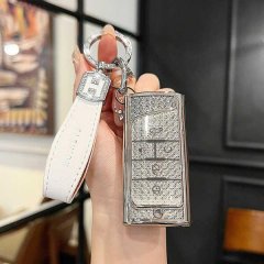 A hand holds a gac trumpchi m8 key cover, featuring a sleek, glittery design with a white leather strap and a silver h charm,...