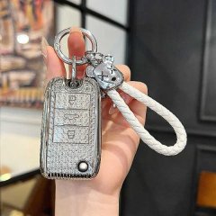 A hand holds a sleek mg6 pro key cover, featuring a textured silver design with a white braided strap and a decorative charm,...